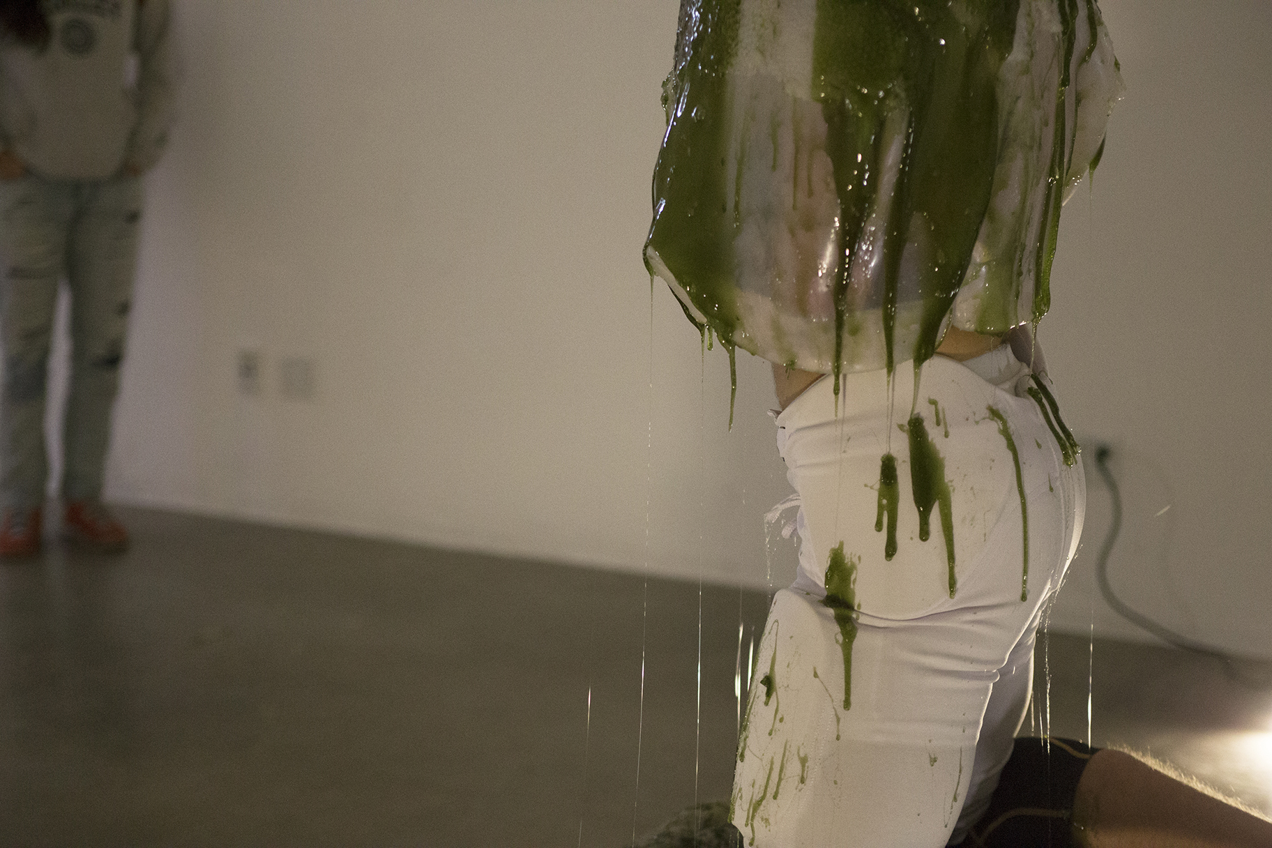 Detail of man engulfed in a gelatenous form covered in tentacles knealing over a pool of green slime in a gallery